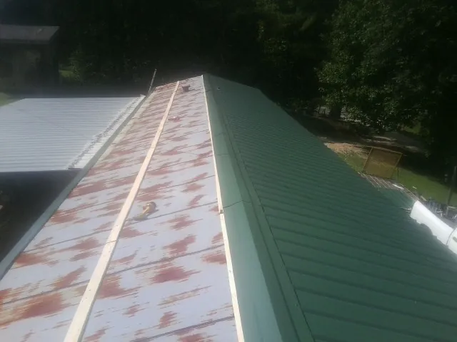 Old rusted panels beside newly installed green metal roofing — Wind Damage Roof Repair by Roofing Brothers in Empire