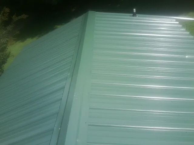 New green metal panels meeting at the ridge of a roof — Flat Roof Repair work by our crew in Empire