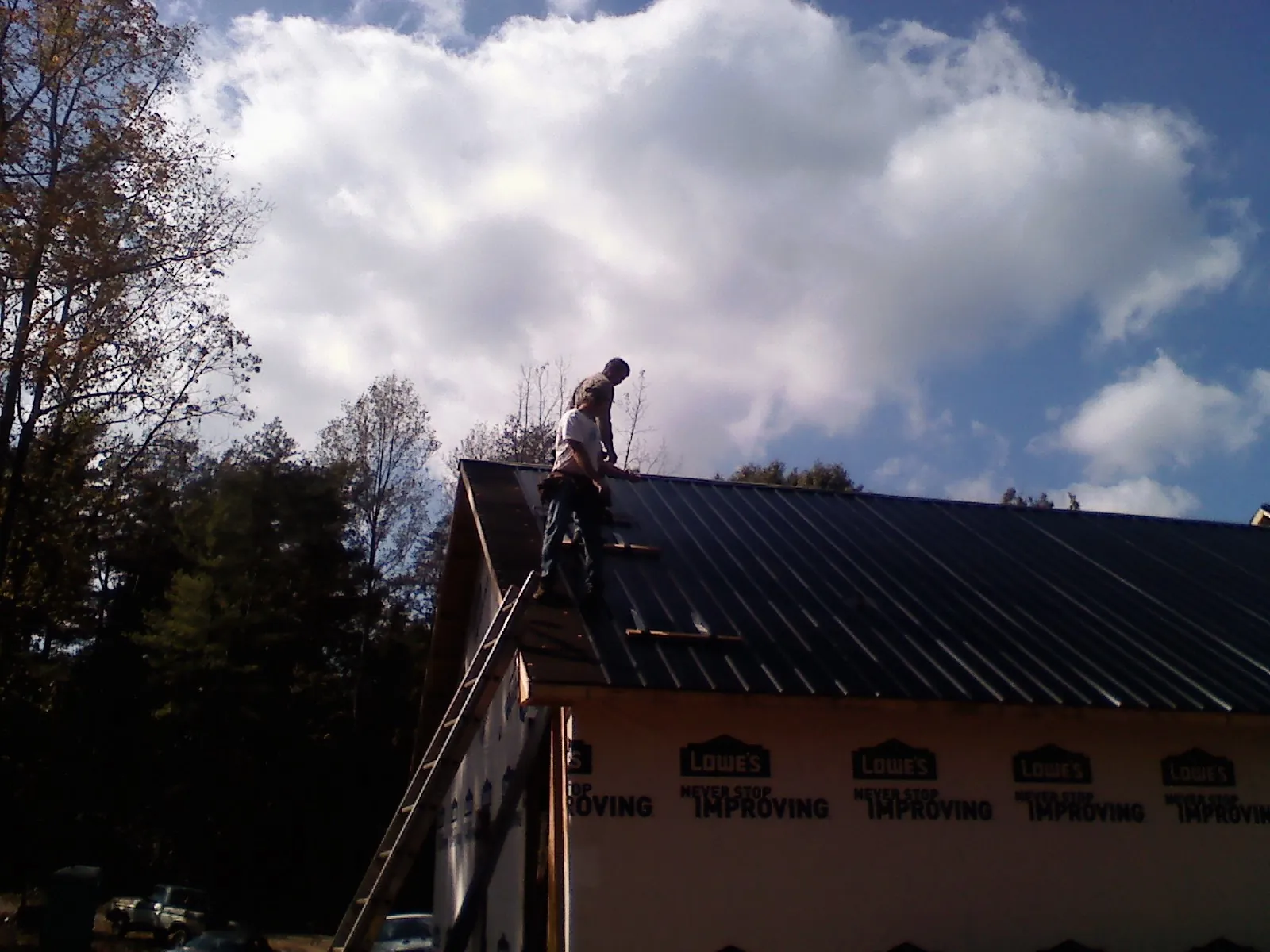 Roofer fastening dark metal panels high against a cloudy sky, from a Roof Inspection job in Empire
