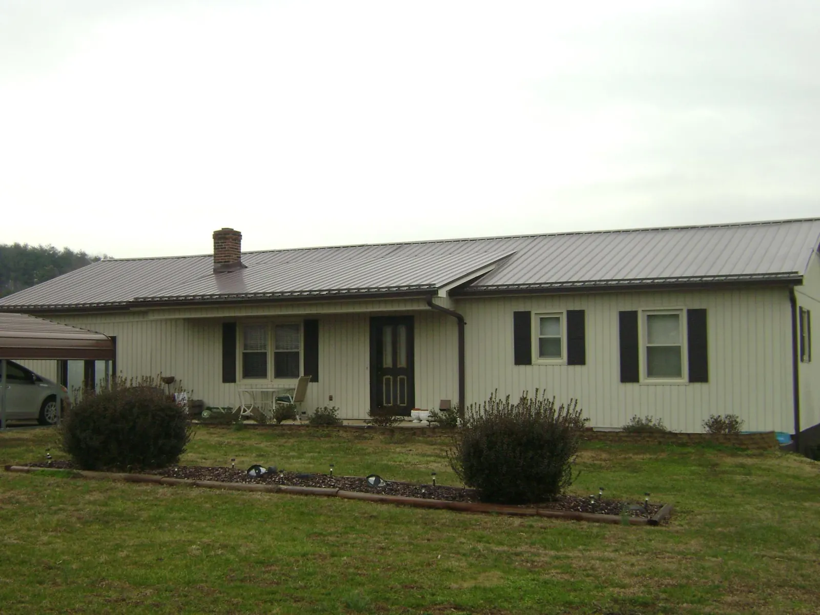 Brown metal roof on a cream sided ranch home with a brick chimney in Empire